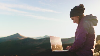 Woman working on laptop in autumn mountain sunset. Girl remote working on notebook. Tourist girl typing on notebook. Hiking, trekking, outdoor lifestyle travel on holiday vacation.