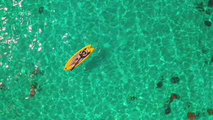 Woman lying on yellow paddle board in open sea. Turquoise water, coral reef, tropical island. Outdoor lifestyle travel on summer holiday vacation. People active sport, relax. Aerial view