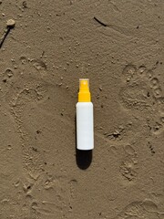 A white plastic spray bottle with a yellow cap placed on wet sand. Minimalist beach-themed composition, suitable for concepts of summer, skincare, sunscreen, vacation