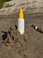 Sunscreen spray bottle with water drops in sand decorated with seashells on the beach, summer vacation concept. Summer holiday background with sun protection concept, skincare product for vacation
