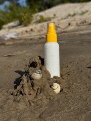 Sunscreen spray bottle with water drops in sand decorated with seashells on the beach, summer vacation concept. Summer holiday background with sun protection concept, skincare product for vacation