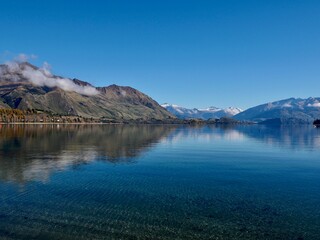 June 2025: Lake Tekapo with snow-capped mountains, autumn trees, and Church of the Good Shepherd under blue sky. Scenic view taken in South Island, New Zealand.