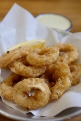 Golden fried calamari rings with lemon wedge and dipping sauces in metal bowl on wooden table. Taken at casual restaurant in Bangkok, Thailand.
