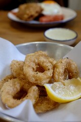 Golden fried calamari served with lemon wedge and dipping sauce in casual Bangkok restaurant, Thailand. Crispy texture and appetizing presentation.