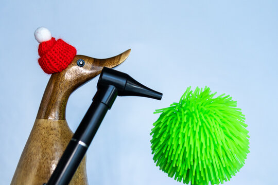 Wooden duck in red hat looks at green spiky ball symbolizing virus.