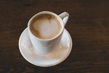 Hot latte coffee in white cup. Cappuccino style latte on table. Cup of latte with frothy milk. Freshly brewed latte with milk foam.