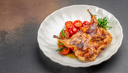 Grilled quail with cherry tomatoes and herbs on a white plate. top view. copy space