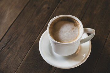 Fototapeta premium Hot latte coffee in white cup. Cappuccino style latte on table. Cup of latte with frothy milk. Freshly brewed latte with milk foam.