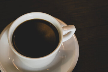 Hot coffee in white mug with dark backdrop. Freshly brewed coffee against black background. Cup of coffee on dark background.