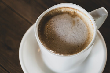 Obraz premium Hot latte coffee in white cup. Cappuccino style latte on table. Cup of latte with frothy milk. Freshly brewed latte with milk foam. Dark background.