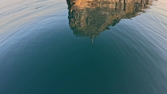 Fishing lure ocean, jigging artificial bait in calm water near rocky cliff reflection.