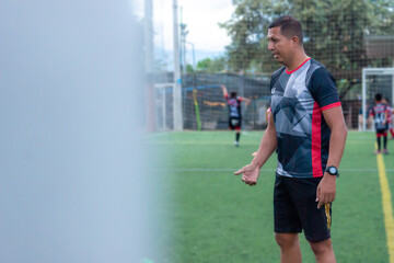 Portrait of a latino male soccer coach giving instructions to students playing on a synthetic field in Neiva, Huila, Colombia. Concept of sports and copy space