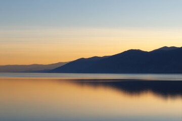 Serene Lake Reflection: A breathtaking landscape showcasing a tranquil lake reflecting the soft hues of a sunrise, with majestic mountains silhouetted in the distance.