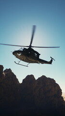 An old American military retro helicopter soaring over a rugged mountain range with snow-capped peaks.