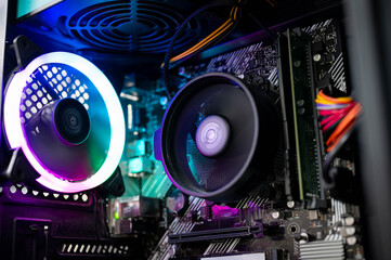 Close-up of colorful RGB cooling CPU fan, motherboard, RAM, and cables inside a custom-built PC desktop, representing modern computer hardware and gaming technology concept.