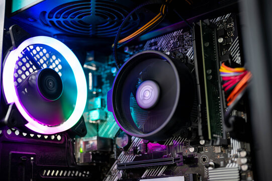 Close-up of colorful RGB cooling CPU fan, motherboard, RAM, and cables inside a custom-built PC desktop, representing modern computer hardware and gaming technology concept.