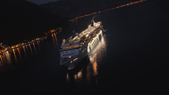 Unique aerial footage of a luxury cruise liner sailing through Kotor Bay near Perast, Montenegro, during blue hour. The drone performs a spiraling orbit with camera roll rotation