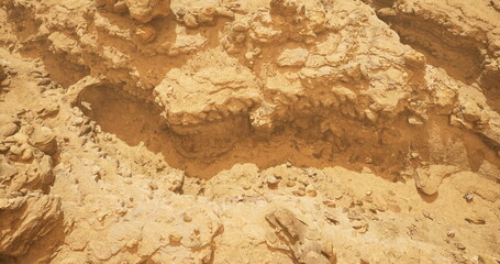 Sunlight illuminates intricate sandstone rock formations in a vast desert. The rugged terrain features various textures and colors, showcasing the natural beauty of the arid environment.