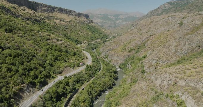 Aerial view of a road winding through verdant mountains alongside a river, contrasting the lush green foliage against the arid landscape, Odzun, Lori Province, Armenia.