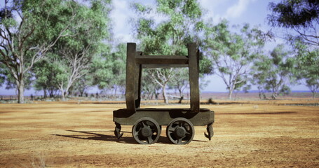 Fototapeta premium A rusty metal cart sits on cracked, dry soil surrounded by sparse trees under a clear blue sky. The landscape indicates a remote area, evoking a sense of abandonment and history.