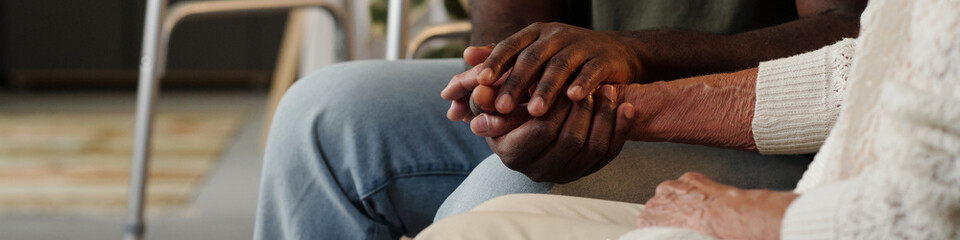 Fototapeta premium Black man holding hands with senior Caucasian woman, offering comfort and support, closeup of intertwined hands showing intergenerational connection and emotional care