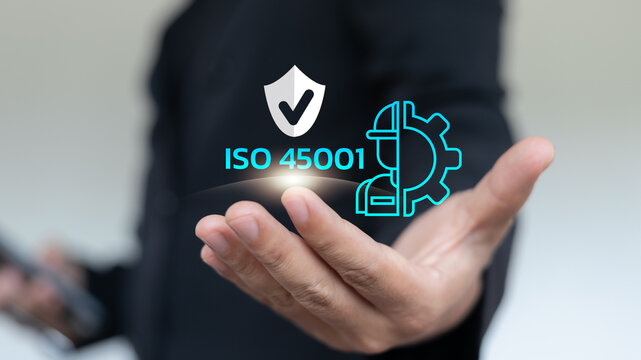 Businessman holding ISO 45001 certification icon with safety shield, helmet, and gear, representing occupational health and safety management system, workplace protection, and risk prevention.