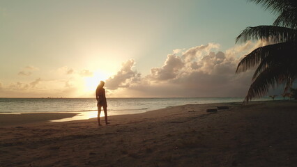 Woman is enjoying a beautiful sunset on the beach, with golden light reflecting off the ocean and...