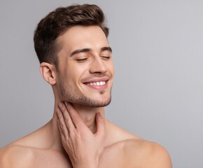 Fototapeta premium A handsome man with a happy expression, touching his neck, displays healthy, glowing skin against a neutral backdrop.