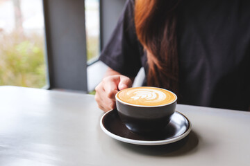 Closeup image of a woman holding a cup of hot latte coffee on the table