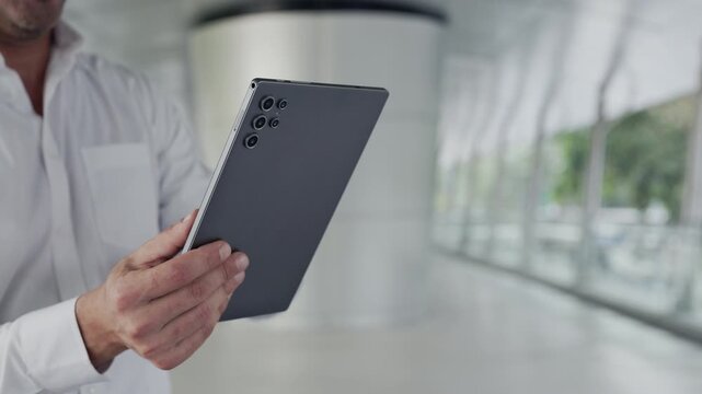 Crop view of entrepreneur hands use modern digital tablet in office. Businessman checks income emails via portable computer device while stands in business center hall closeup