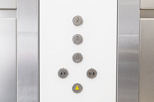 Elevator control panel with metallic buttons and yellow alarm bell. Closeup of floor selection and door operation keys in modern lift interior. Minimal design of stainless steel elevator wall. - Powered by Adobe
