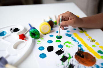 Child painting with bright colors using sponge brushes on white canvas
