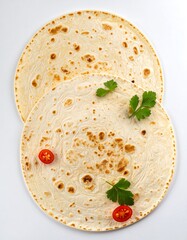 Two round flatbreads, adorned with fresh parsley and cherry tomatoes, sit stacked atop one another against a bright background.