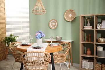 Stylish setting with plates and vase of flowers on wooden table in dining room. Interior design