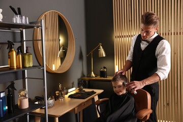 Professional barber working with little boy in barbershop