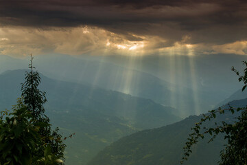 Sun rays coming out of cloud burst - at Rabangla, Sikkim, India. Slihoutte trees in foreground and...