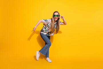 Beautiful young woman posing in a stylish casual outfit with sunglass against a bright yellow background showcasing a cheerful mood