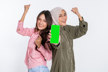 Two joyful friends showing a smartphone with a green screen, celebrating together.