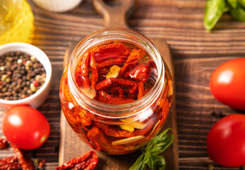 Dried organic tomatoes preservation with herbs and olive oil in jar.