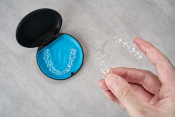 Clear dental aligner in hand and blue case on marble table. Dental orthodontic mouthpiece.