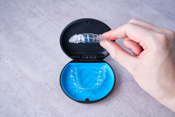 Clear dental aligner in hand and blue case on marble table. Dental orthodontic mouthpiece.