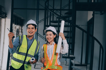 Construction manager and engineer dressed in orange work vests and hard helmets explore construction documentation on the building site near the steel frames
