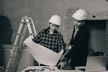 Construction manager and engineer dressed in orange work vests and hard helmets explore construction documentation on the building site near the steel frames