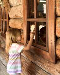 A child looks into the window of a wooden house.