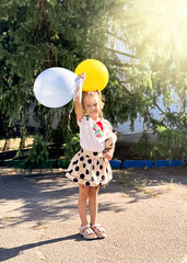A girl plays on the street with balloons in the colors of the Ukrainian flag, wearing an embroidered shirt.
