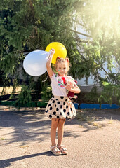 A girl holds two balloons, yellow and blue, at a summer party.