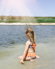 The girl sits in the water and looks into the distance.