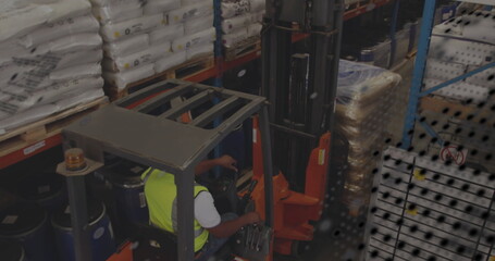 Forklift operator wearing safety vest loading pallets in warehouse, with metal racks and blue drums