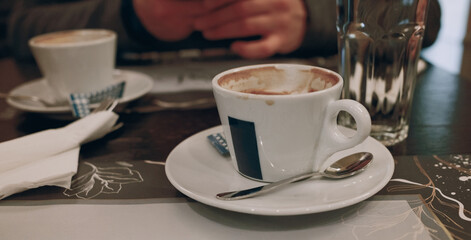 A close-up of two empty coffee cups on a saucer with spoon, served at a cozy cafe table. Date in cafeteria