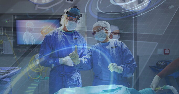 Two surgeons in scrubs gesturing to holographic interface above table in operating room
